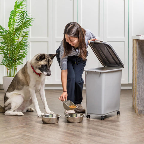 Woman using Portable 40Lb Pet Food Storage Bin With Wheels, Airtight Lid, Built In Scoop In Lid, BPA Free, Durable Gray Dog Food Organizer