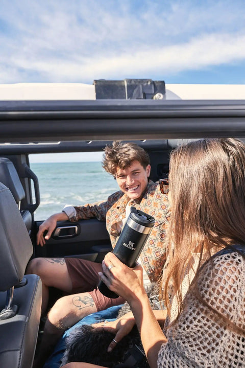 Woman holding 20 Oz Leakproof Stainless Steel Travel Bottle With Locking Lid in car at beach, ideal for coffee or water on the go.