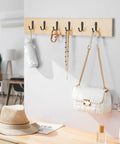 Image showing a wooden board with five black metal 10 Pack Wall Hooks For Bathroom Kitchen Closet And Garage Black Metal Hangers That Hold Up To 40 Lbs Ultra Strong Built To Last Great For Coats Towels Hats Keys Bags And Coffee Cups Modern Durable Design mounted on a wall, holding a white handbag, necklaces, a keychain, and a rolled umbrella, kitchen interior visible.