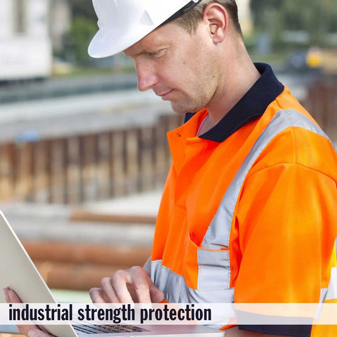 Construction worker in orange safety vest and white helmet using a laptop on a building site.