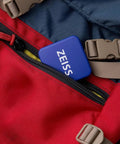 ZEISS lens cleaning tin boxes with hinge lids, blue, pack of 4, tucked into a red backpack pocket.