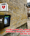 Kigley AED projection sign and portable cabinet mounted on brick wall; white sign with red heart and black cabinet with AED label.