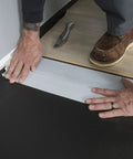 Person installing Straight Shooter Floor Underlayment For Laminate And Engineered Wood, 600 Square Foot Roll on black subfloor.