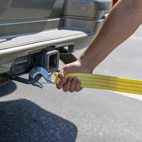 Person attaching Heavy Duty Tow Strap With Hooks, 2 Inch By 20 Foot, 10,000 Pound Capacity, Bright Yellow Polyester Webbing to vehicle hitch