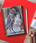 Spiral notebook with bird sketch, accompanied by a white pencil from the White Charcoal Pencil Set Six Pack For Dark Paper Highlights And Sketching Pro Grade Blendable Pencils For Drawing Shading And Blending Beginners To Artists Dope Quality, on a wooden table with red paper and gift boxes.