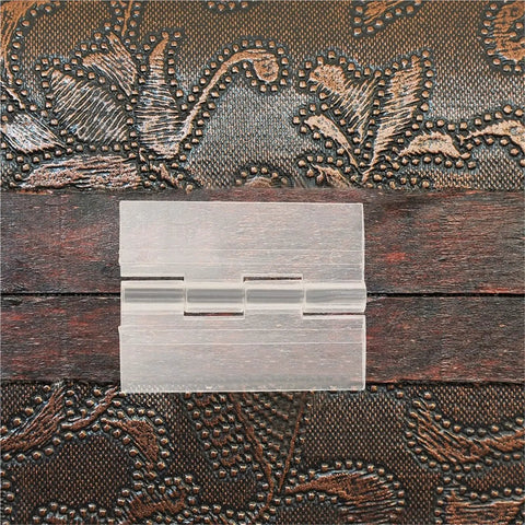 Close-up of 5Pcs Transparent Self Adhesive Cabinet Hinges For Small Boxes And Piano Lids on a decorative wooden surface.