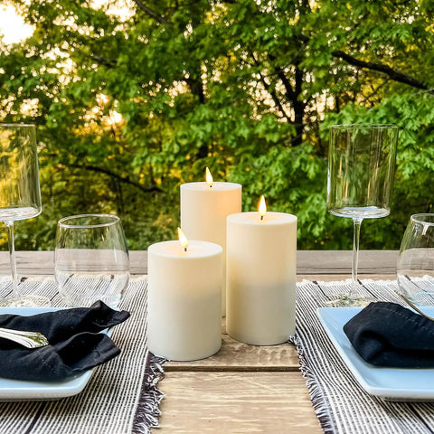 Waterproof Outdoor Flameless Pillar Candles 3 Pack In Ivory Resin, 3x4, 3x5, And 3x6 Inches on a patio table setting
