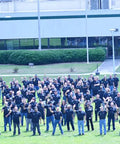 Large group of people on grass field in front of a building on a sunny day