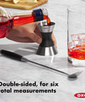 Stainless Steel Two Sided Jigger With Flip Measurements in use, soft non slip grip, pouring red liquid, ice-filled glass nearby.