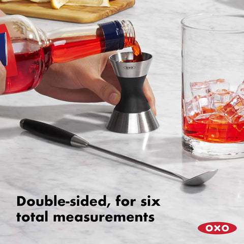 Stainless Steel Two Sided Jigger With Flip Measurements in use, soft non slip grip, pouring red liquid, ice-filled glass nearby.