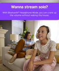 Girl with headphones enjoying a show on a couch while adult reads nearby, showcasing Next Level HD Media Stick Player With Clutch Voice Remote For Smooth Streaming Of Live TV Free Movies And Your Favorite Apps Designed For Zero Hassle Plug And Play Everyday Setup.