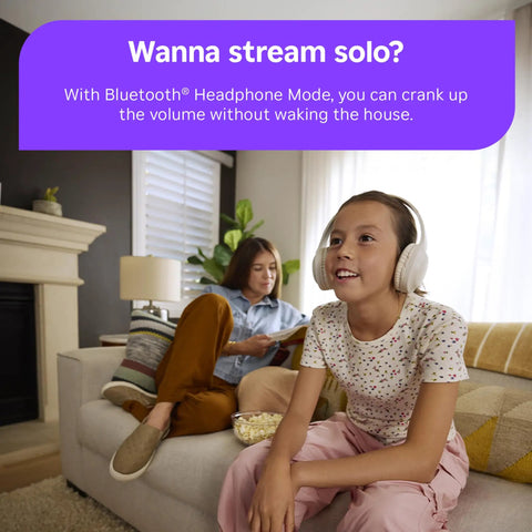 Girl with headphones enjoying a show on a couch while adult reads nearby, showcasing Next Level HD Media Stick Player With Clutch Voice Remote For Smooth Streaming Of Live TV Free Movies And Your Favorite Apps Designed For Zero Hassle Plug And Play Everyday Setup.