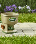 Hand Powered Lawn Spreader for Grass Seed Fertilizer Salt Ice Melt with Adjustable Arm Support on stone path