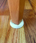 Super Grippy Rubber Furniture Cups To Kick Sliding And Scratching Away Straight Up Heavy Duty Floor Protectors For Chairs Tables And Caster Wheels Up To One And Half Inch Size With Easy Four Pack Setup under a wooden chair leg on hardwood floor.