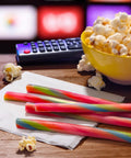 Ropes Candy Twisted Rainbow Punch Flavor Soft And Chewy 9 Oz Pack with popcorn and remote on a table.