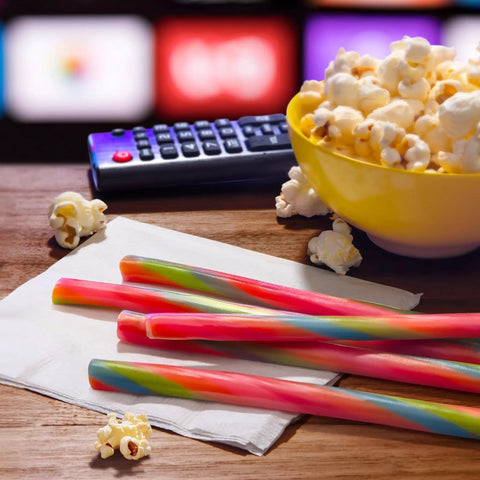 Ropes Candy Twisted Rainbow Punch Flavor Soft And Chewy 9 Oz Pack with popcorn and remote on a table.