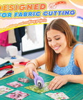 Woman using a pink Rotary Cutter For Fabric With 45mm Blades And 5 Extra Replacement Blades, fabric pieces on table.