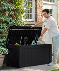 Man using 120 Gallon Outdoor Deck Box Heavy Duty Resin Construction Weatherproof Lockable Storage For Patio Furniture Garden Tools