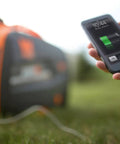 Hand holding a charging smartphone connected to a Quiet Portable Inverter Generator With Gas Powered 2000 Watt CARB Compliant Clean Electricity.
