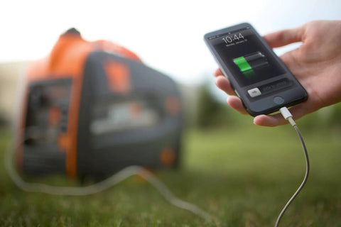 Hand holding a charging smartphone connected to a Quiet Portable Inverter Generator With Gas Powered 2000 Watt CARB Compliant Clean Electricity.