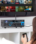 Home Audio Power Amplifier System 2x40W Bluetooth Mini Dual Channel Mixer next to TV with remote control in hand