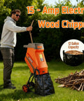 Man using a 15 Amp Electric Wood Chipper Shredder with Collection Bag and Push Stick on a grassy lawn, pile of branches nearby.