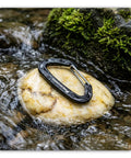 Heavy Duty 15kN Wire Gate Carabiner on rock in stream, aluminum quick draw clip for camping and hiking, black anodized finish.