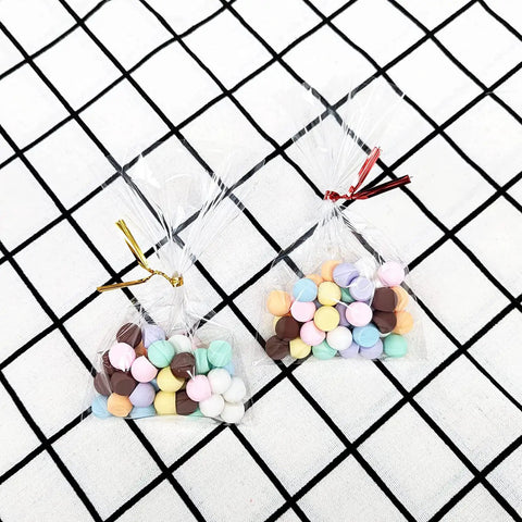 Clear 4x6 Cellophane Bags With 4 Inch Twist Ties, 100 Pack, 1.4 Mil OPP Treat Bags holding colorful candies on a checkered background