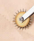 Close-up of a metallic tracing wheel perforating fabric, part of Two Pack Tracing Wheel and Pounce Wheel Set for Paper Perforation and Pattern Making