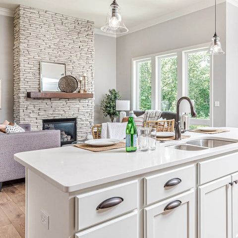 Modern kitchen with white island, overhead pendant lights, and view of cozy living room with stone fireplace.