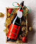 Gift box with a bottle wrapped in Four Rolls Christmas Metallic Bakers Twine 110 Yards Each Gold Silver Red Green For Gift Wrapping Game And DIY Crafts Durable Jute String Pack Of Colorful Twine For Packaging Materials And Decor, adorned with red and green twine, and decorative ornaments on wood background.