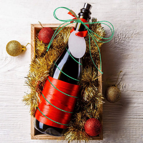 Gift box with a bottle wrapped in Four Rolls Christmas Metallic Bakers Twine 110 Yards Each Gold Silver Red Green For Gift Wrapping Game And DIY Crafts Durable Jute String Pack Of Colorful Twine For Packaging Materials And Decor, adorned with red and green twine, and decorative ornaments on wood background.