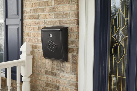 Locking Wall-Mounted Mailbox In Rubbed Bronze on brick exterior next to door, decorative embossed design visible