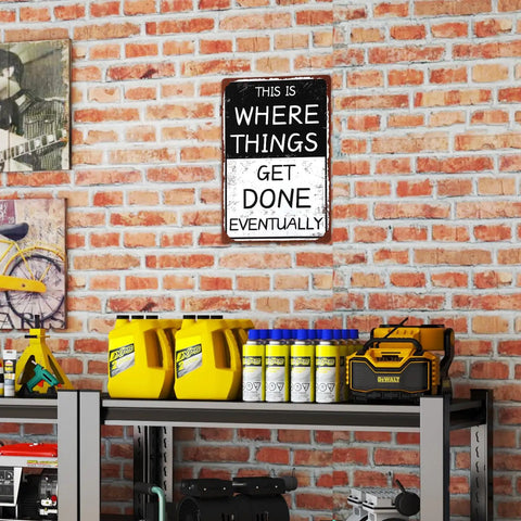 Funny Garage Sign This Is Where Things Get Done Eventually Vintage Metal Tin Wall Decor displayed on a brick wall above workshop shelves