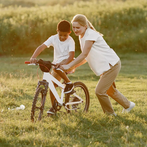 Child learning to ride a bike on grassy field, adult assisting, showcasing Two Pack 20x1.75 to 2.125 Inch Bike Inner Tubes With AV32mm Schrader Valve