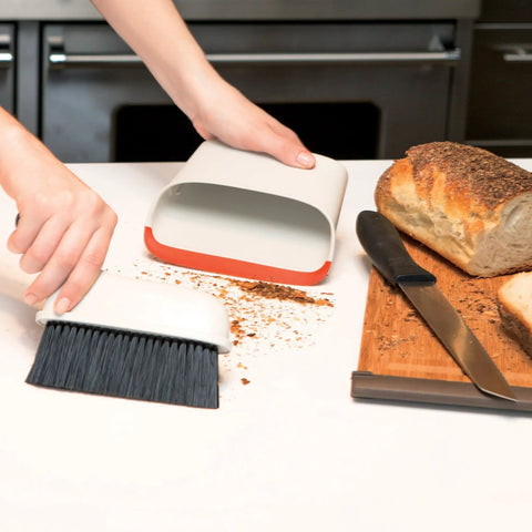 Compact Dustpan And Brush Set With Snap In Design And Bristle Cover cleaning crumbs on countertop near bread