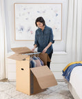 Woman using Heavy Duty Tape Free Wardrobe Moving Boxes 3 Pack With Sturdy Hanging Rail And Grippy Handles to pack clothes.