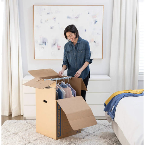 Woman using Heavy Duty Tape Free Wardrobe Moving Boxes 3 Pack With Sturdy Hanging Rail And Grippy Handles to pack clothes.