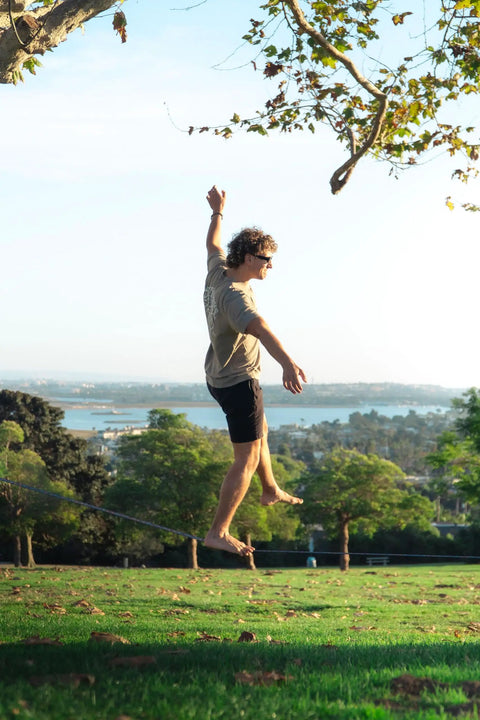 Person balancing on 1 Inch Slackline Kit With Dual Ratchet System 82 Foot Jungle Line Webbing Two Tone Design To Eliminate Twists