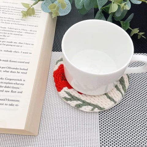 White mug on punch needle coaster from Punch Needle Coaster Kit With 6 Dope Floral Patterns on table with book and greenery.