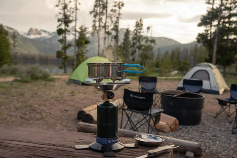 Portable Propane Stove With 10,000 BTU Burner chrome anti-clog design in campsite setting with pots and tents, ideal for outdoor use