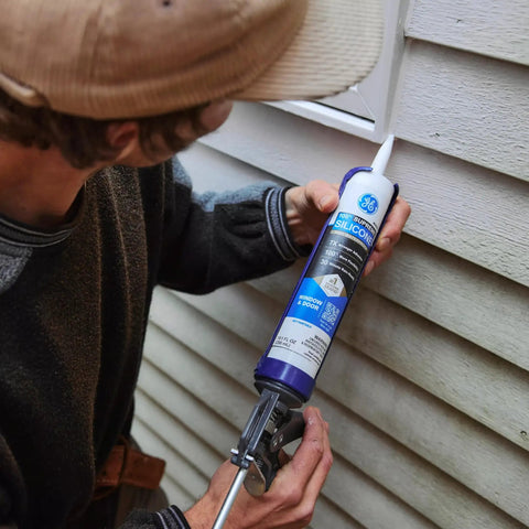 Person applying All Purpose Silicone Caulk Clear 10 Fl Oz Cartridge 12 Pack 100 Percent Waterproof Sealant to exterior siding