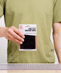 Person holding Tenacious Tape Repair Patches Peel And Stick Nylon Gear Patches For Jackets Tents Sleeping Bags Backpacks In Black