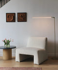 Libra LED Floor Lamp With Adjustable Pivot Arm And Built In Dimmer beside a modern chair and round table, sleek brass design