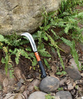 Weeding Sickle For Gardens And Lawns leaning against ferns, ergonomic hand sickle with grip, sharp carbon steel blade visible.