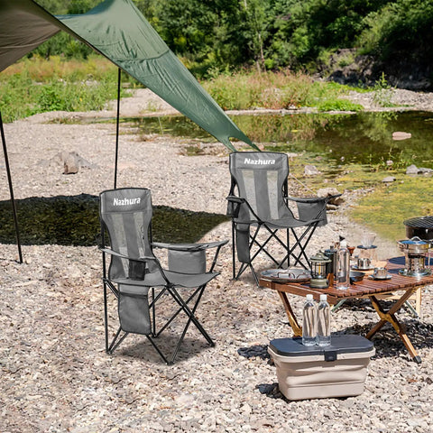 2 Pack Foldable Outdoor Camping Chairs with Built In Cooler Pouch Ultra Comfy Cushioned Seats Mesh Backrest and Cup Holder Pocket in Grey set up by a riverside with picnic equipment.