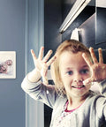 Child with raised hands in front of a mounted hands free Z Wave gesture controller for smart homes, no touch swipe pad visible.