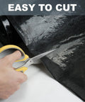 A hand holding scissors cutting the Rock Solid Self Adhesive Rubber Roofing Membrane Roll 39 By 164 Feet Waterproof Leak Tape in black.