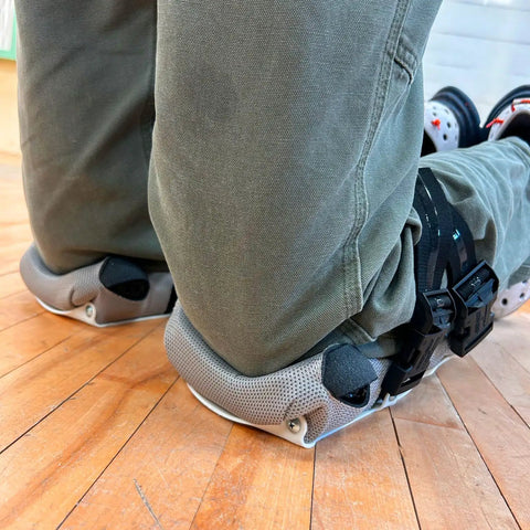 Person kneeling on hard floor wearing All Purpose Kneepads With One Inch Foam Cushion Inserts For Maximum Comfort And Joint Support Non Slip 3 Ply Frame With Live Hinge For A Fit Like A Glove One Size Fits All In White Or Black.