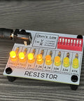 Hands On Soldering Practice Kit resistor board with LED lights, Ohm's Law diagram, and DIP switch on gray surface